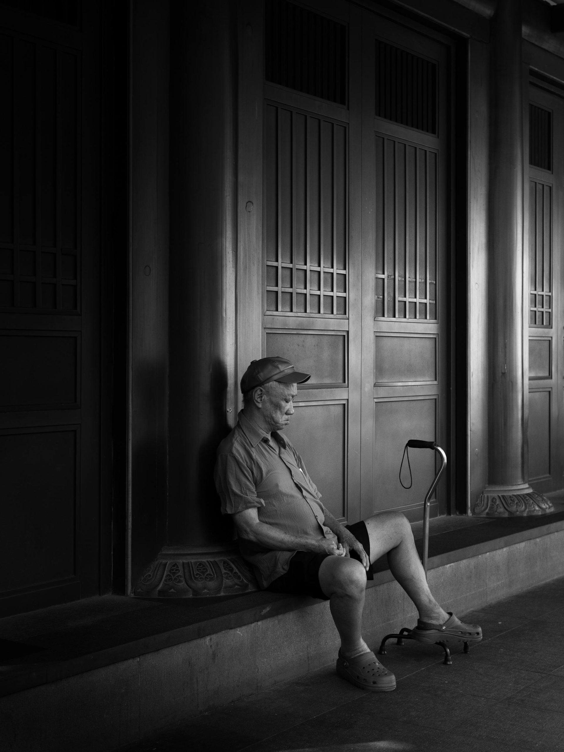 The old man is sitting on the ground with a canes next to him